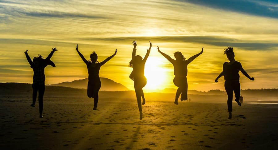 Five people jumping joyfully on a beach at sunset, silhouetted against a golden sky.